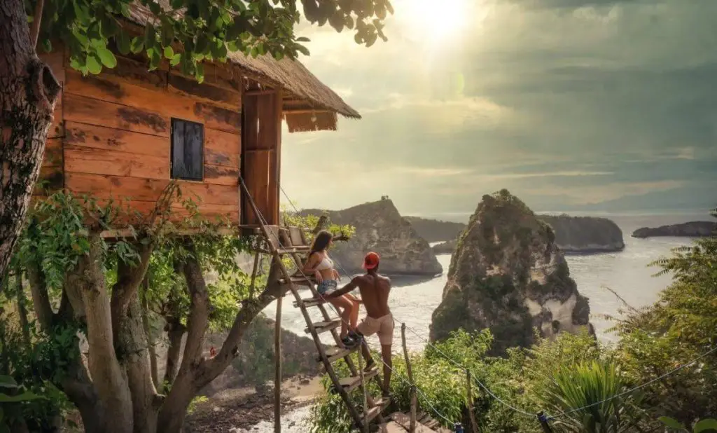 travel love relationship a couple stand on the ladder of a beach hut in bali looking at the water and islands. happytogetheranywhere.com