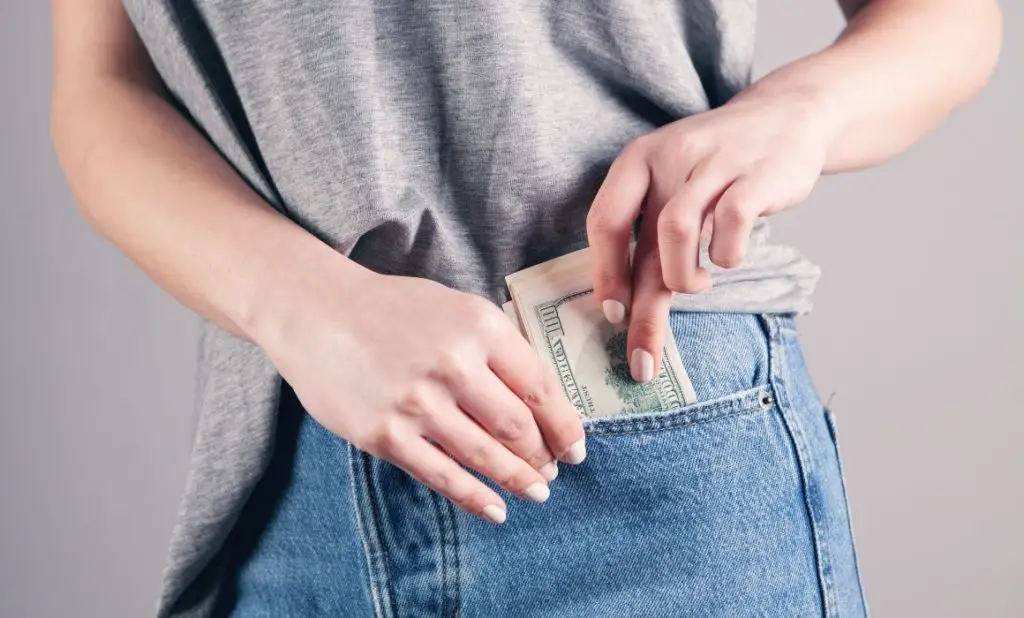 a woman tucking cash in her front jeans pocket. happytogetheranywhere.com