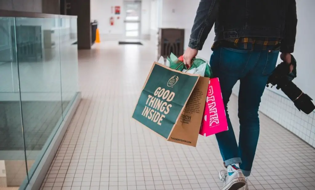 a man carries shopping bags that say good things inside walking in a hall. happytogetheranywhere.com