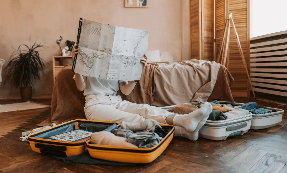 woman learning how to plan a long trip as she sits on the floor between packed suitcases reading a map