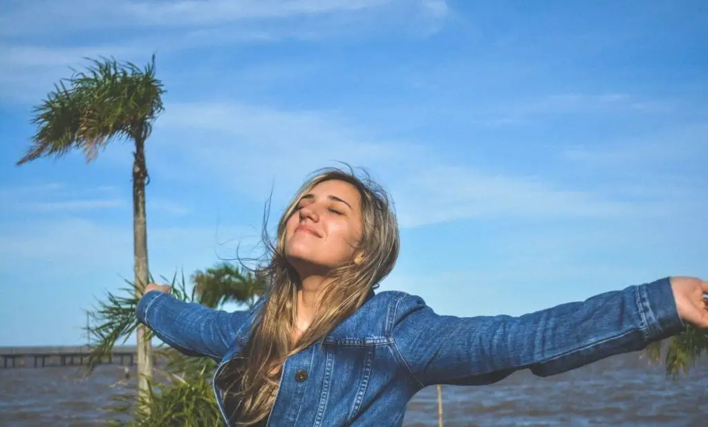 grateful for a beautiful day a blonde female in blue denim jacket raises face to the sun with arms spread wide. happytogetheranywhere.com