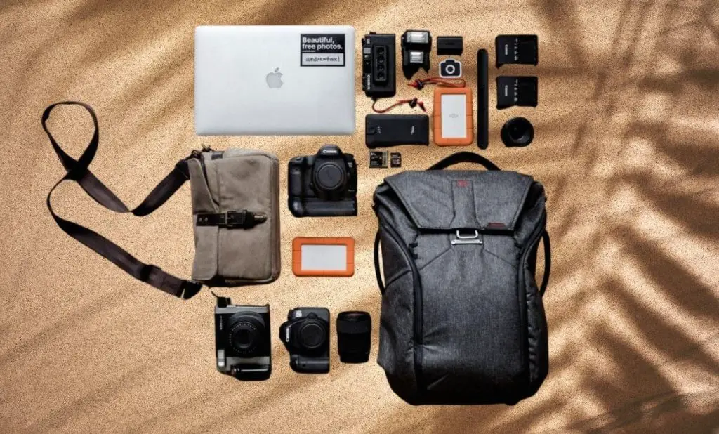packing list for southeast asia photo of backpack, camera, laptop and other electronics on the beach. happytogetheranywhere.com