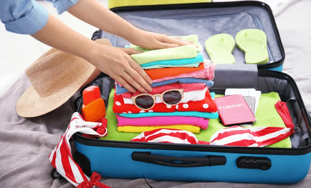 woman packing a small blue suitcase with bright vacation clothes and passports as she prepares for a long trip. happytogetheranywhere.com