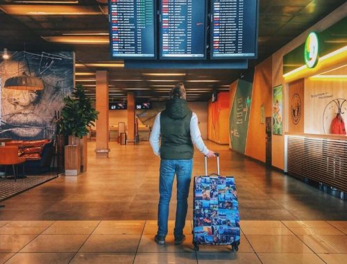 top reasons to travel man looking at airport departure screen with blue suitcase
