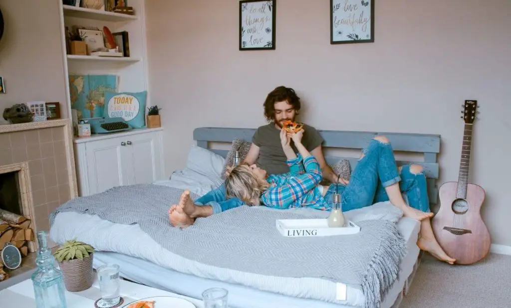 woman feeding pizza to a man in bed. happytogetheranywhere.com